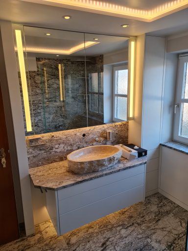 Exklusives Badezimmer mit Naturstein-Waschtisch, Aufsatzwaschbecken und großflächigem beleuchteten Spiegelschrank
